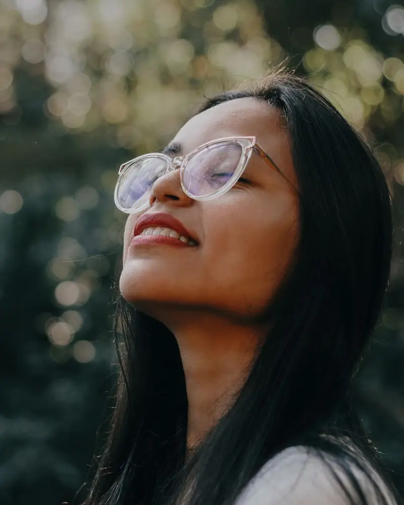 Mulher de óculos com o rosto ao sol, entre as árvores (foto ilustrativa)
